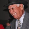 Native American man with short gray hair smiling in hat and suit