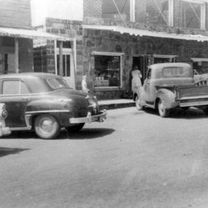 Woman and child outside stone-walled shop with parked cars