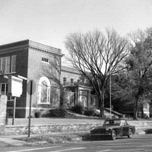 Two-story brick building with trees and parked cars