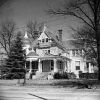 multistory wood frame Victorian home with steeples two chimneys porches with a large conifer and iron fence