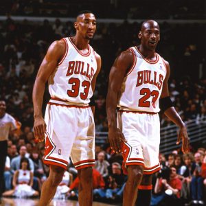 Two black men walking together on the court in NBA Bulls uniforms numbers 33 and 23 with fans in background