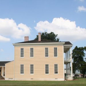 Side view of two-story house with balcony covered porch and single-story rear wing behind it