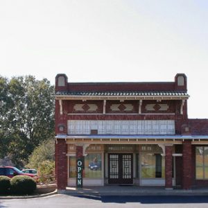 Front view of two-story brick building with single-story extension with sign and parking lot on its left side and flagpole on its right