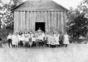 Group portrait white school children with teachers outside wood-frame gabled building