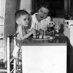 White boy in body brace and white woman playing with toys at small table