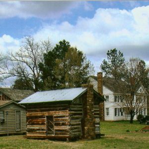 Single-story cabin and outbuildings with multistory house with covered porch and balcony in the background