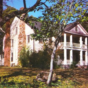 Wood frame mansion with porch, balcony, double chimneys, foreground foliage