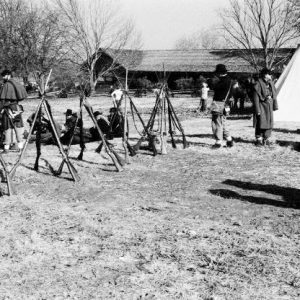 Civil War reenactors  in field near cabin & teepee with five groups of stacked rifles