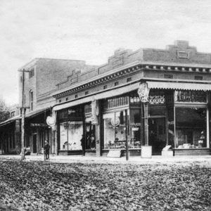 City block with dirt road corner brick drug store two white women in dresses bonnets