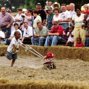 Black boy Smiling and running with small tiller on dirt track with  audience watching