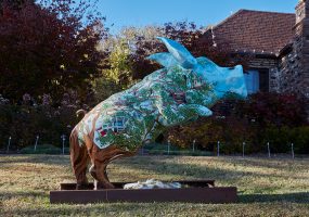 Trees and buildings painted on hog sculpture with brick building in the background