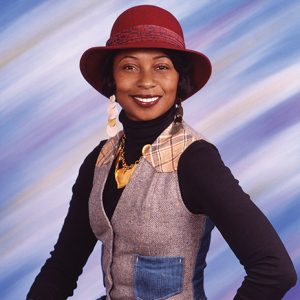 Young African-American woman smiling in hat and vest over long sleeve shirt