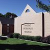 Brick building and modern brick "Rogers Historical Museum" building with bushes lawn flag pole with American flag