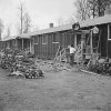 Four Asian-American men construct front porch awning on housing unit opposite stacks of firewood