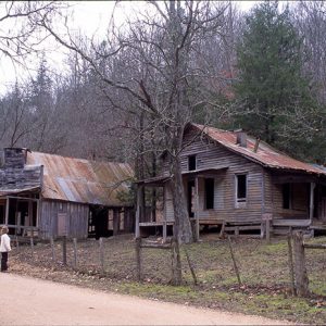 Abandoned wooden house and store on dirt road with fence