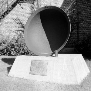 Large kettle pot standing vertically on base with "Salt Kettle" plaque outside brick building