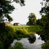 smooth creek runs in front of fields with wooden buildings