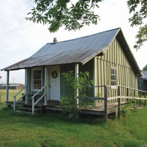 small green wooden building with white door, other buildings in background