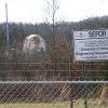 Domed building seen through bare trees beyond a barbed wire fence with sign