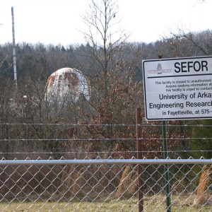 Domed building seen through bare trees beyond a barbed wire fence with sign