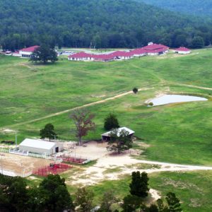 Aerial view of a large field among mountains with building complex opposite barns corral and pond