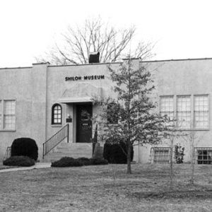 Stucco building with "Shiloh Museum" sign with front steps sidewalk bushes lawn flagpole and bike rack