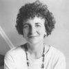 White woman with curly hair wearing beaded necklace