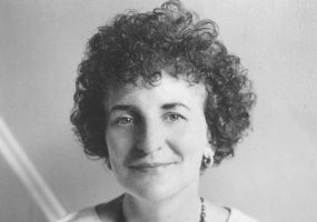 White woman with curly hair wearing beaded necklace