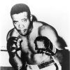 Portrait African-American male boxer with gloves raised, shorts, boots, in corner of ring