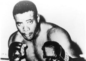 Portrait African-American male boxer with gloves raised, shorts, boots, in corner of ring