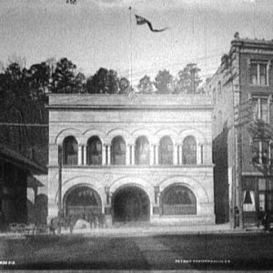 Two-story building with arched windows and arched entrance amid other city buildings