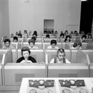 young white men and women seated in cubicle rows in headphones with microphones