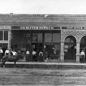 Exterior stone and brick building with sign "Lichlyter News Co.," "Post Office Springdale Ark." with onlookers and horse-drawn carriage