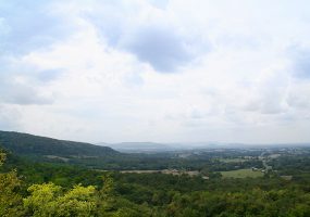 View looking over tree covered countryside with farmland and mountains in the background