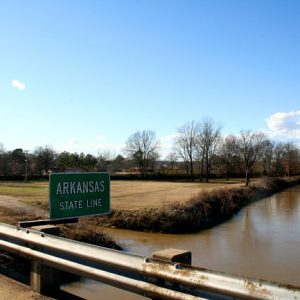 sign next to river "Arkansas State Line"