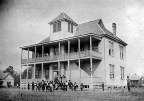 Children in yard outside large two story building with two women on balcony