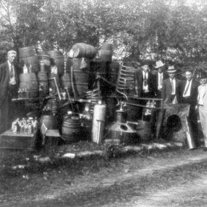 White men in suits posing with large stills, barrels, and bottles