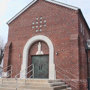 Multistory brick building with framed arch entrance and cross on its roof