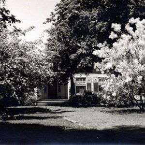 Wood frame home with porch, moon shutters front walkway dense trees and shrubs