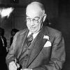 Older white man wearing glasses in suit and tie signing a piece of paper with a pencil