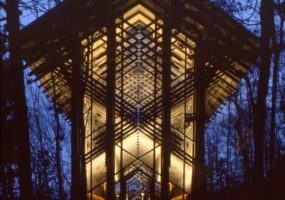 Lighted glass-walled chapel at night with trees
