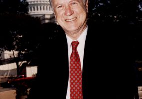 white man in suit and tie with backdrop of state capitol