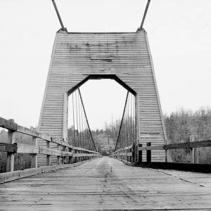 Wood frame bridge with wooden archway and steel cables viewed end to end with forest background