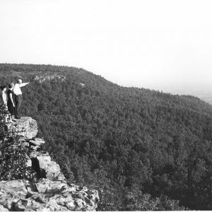 White man and two women standing on a cliff with mountain in the distance