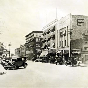 Street lined with signs, power lines, and buildings with parked cars