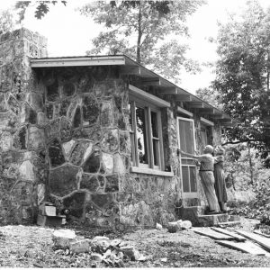 Old man and woman hanging a door on their stone house