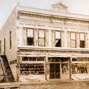 Two-story storefront called "The Right Place" with items in the windows and stairs on the left side next to a small shack