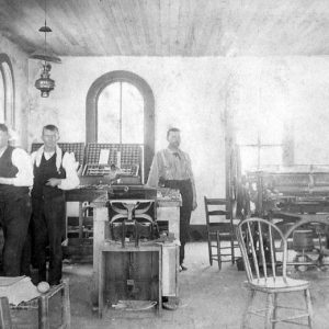 Three white men at work in a printing room with arched windows