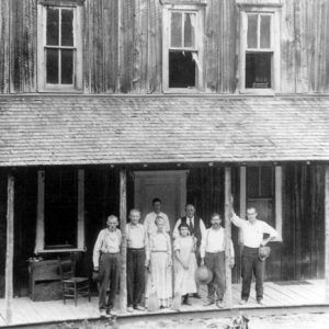 Group of white men and women pose in front of two story building