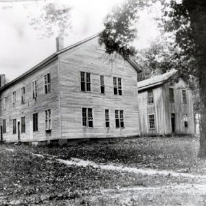 Two large two story wood frame buildings among trees dirt path in foreground